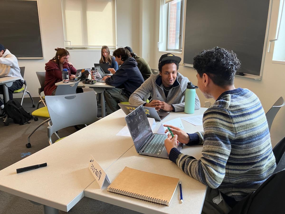 Students sitting in groups at tables discussing classwork